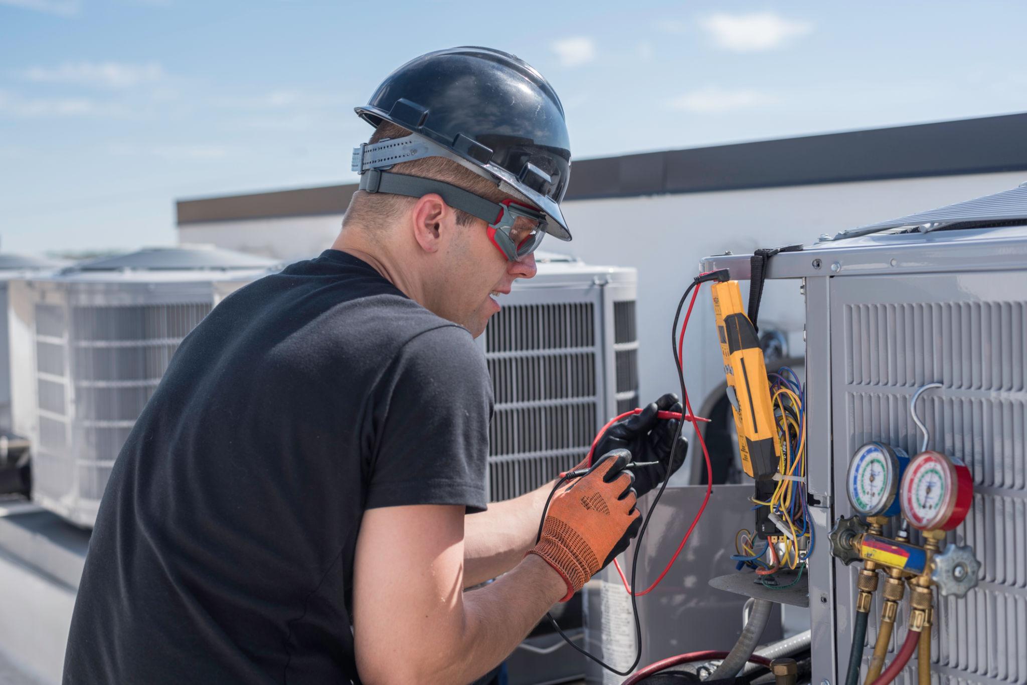 HVAC technician performing seasonal inspection on rooftop air conditioning unit using diagnostic tools to check refrigerant levels and system performance