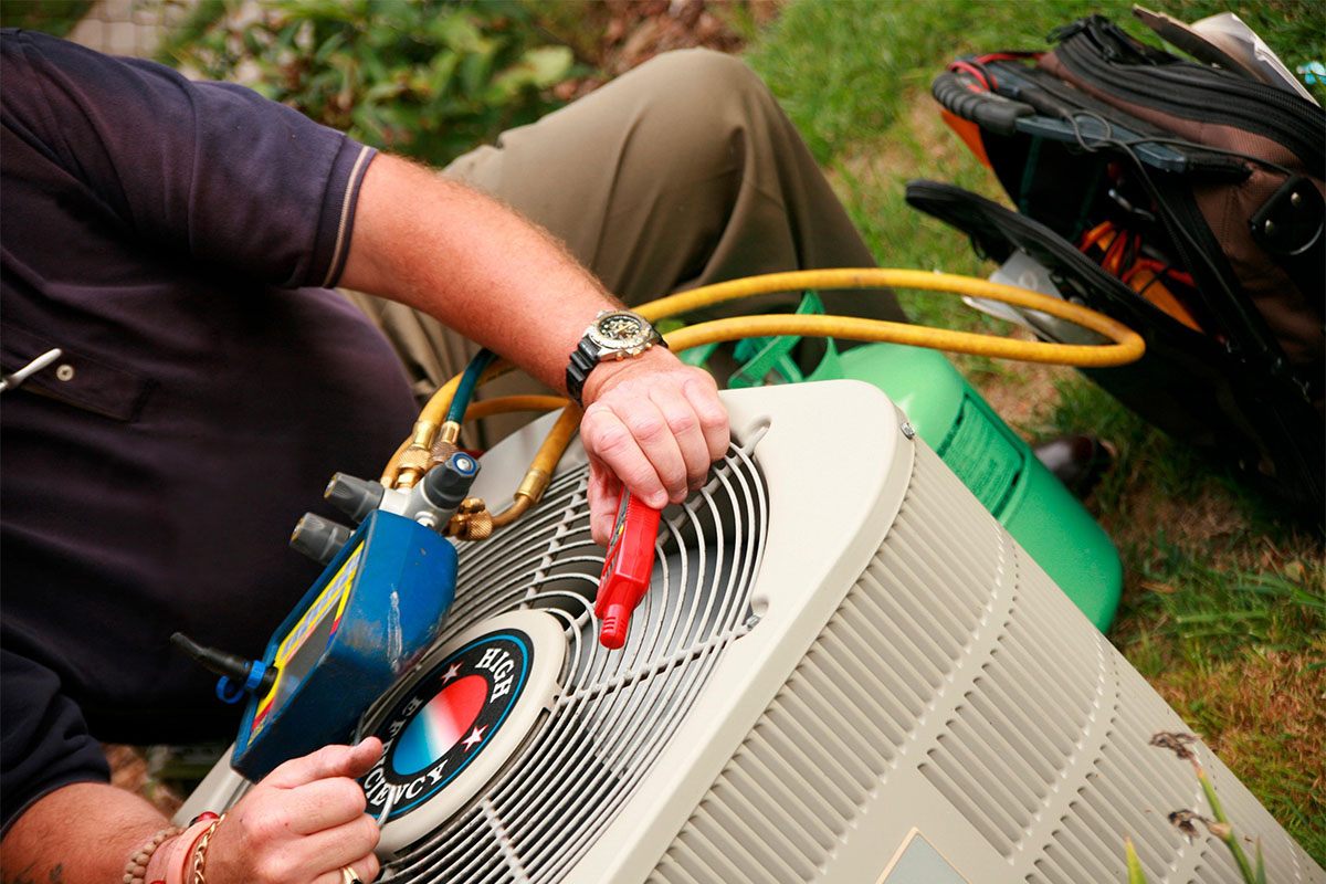 Close-up of a professional HVAC technician using digital manifold gauges and a refrigerant tank to perform an AC refrigerant recharge and diagnostic on an outdoor condenser unit.