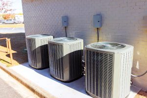 Three modern outdoor central air conditioning units installed next to a brick home, featured on Air Alliance Heating & Cooling's guide on choosing the right AC system for maximum summer comfort in Cottleville, MO.