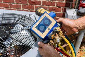 HVAC technician using a digital manifold gauge to test refrigerant pressure levels on an outdoor air conditioner unit.