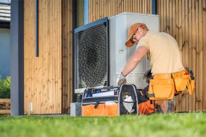 Professional HVAC technician kneeling next to an outdoor heat pump air conditioning unit performing routine repair and maintenance.